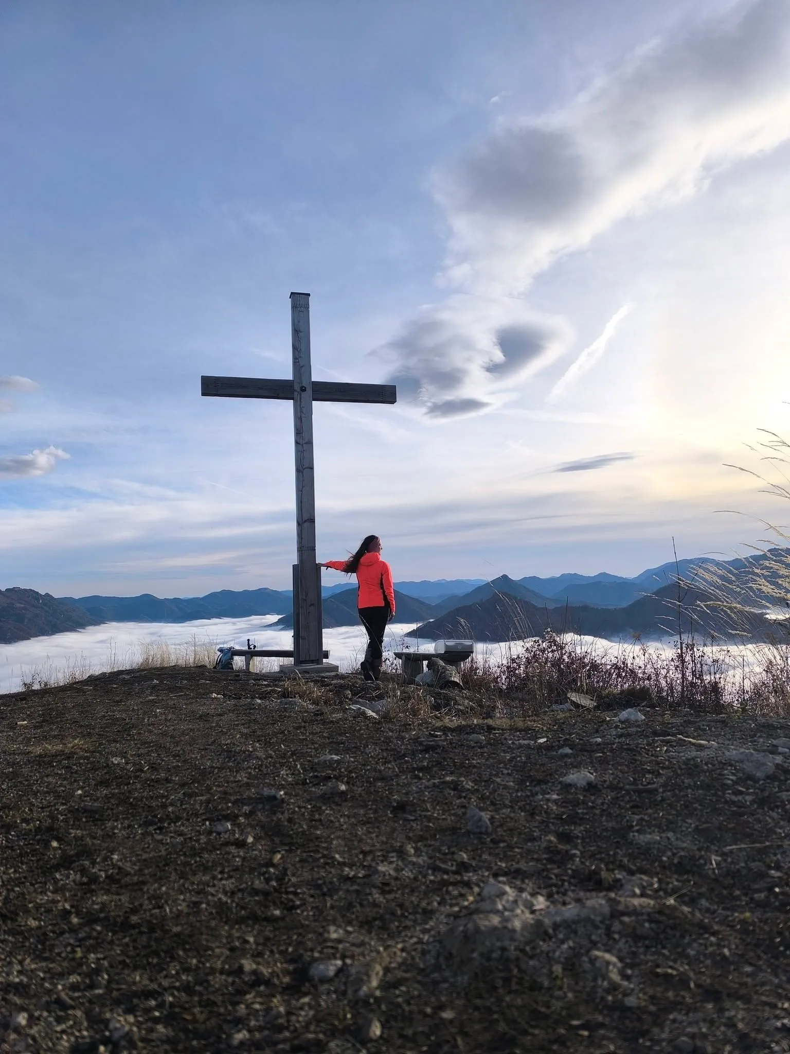 Jennifer allein am Gipfelkreuz über einem geschlossenen Nebelmeer