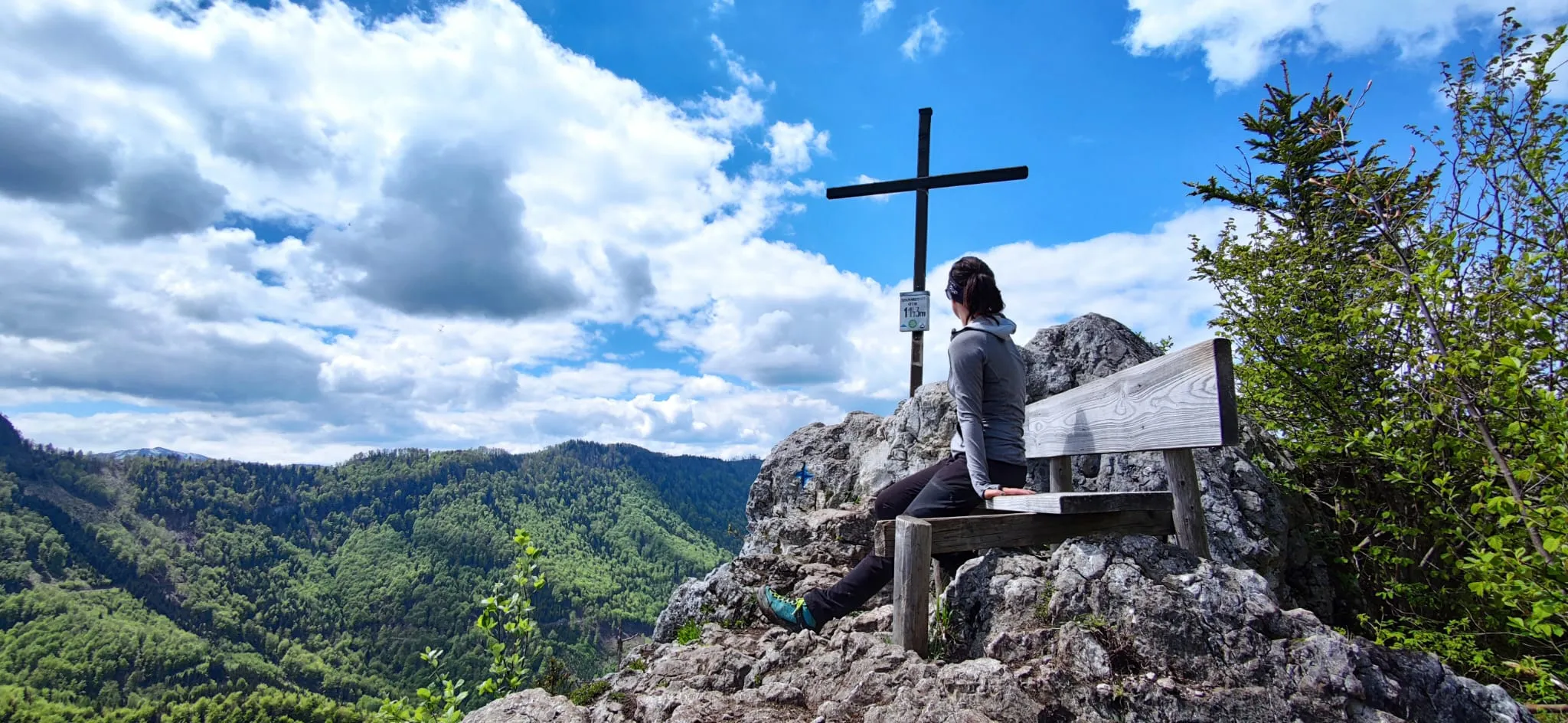 Jennifer auf der Bank am Gipfelkreuz, Blick ins bewaldete Tal — angekommen