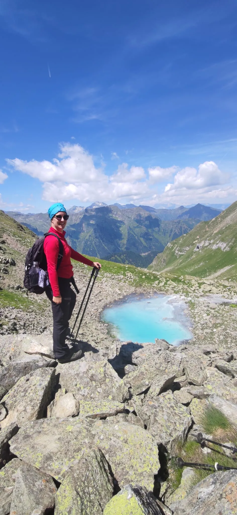 Jennifer mit Stöcken hoch über einem türkisen Bergsee im felsigen Hochgebirge
