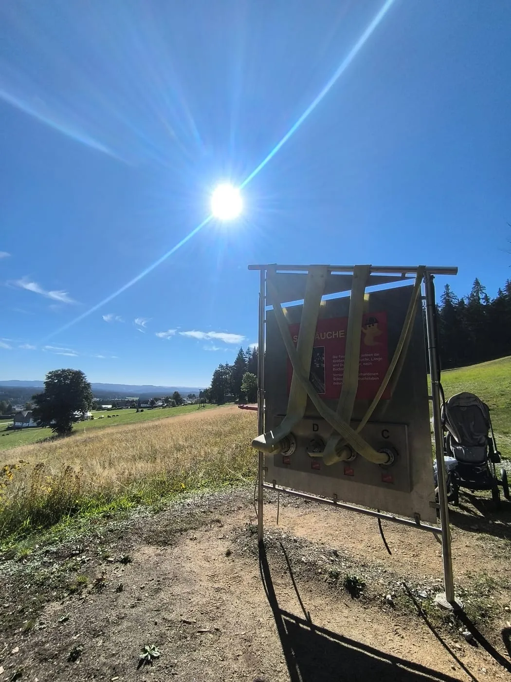 Station mit Seilen und Schläuchen, daneben ein Kinderwagen, dahinter der Blick ins Tal